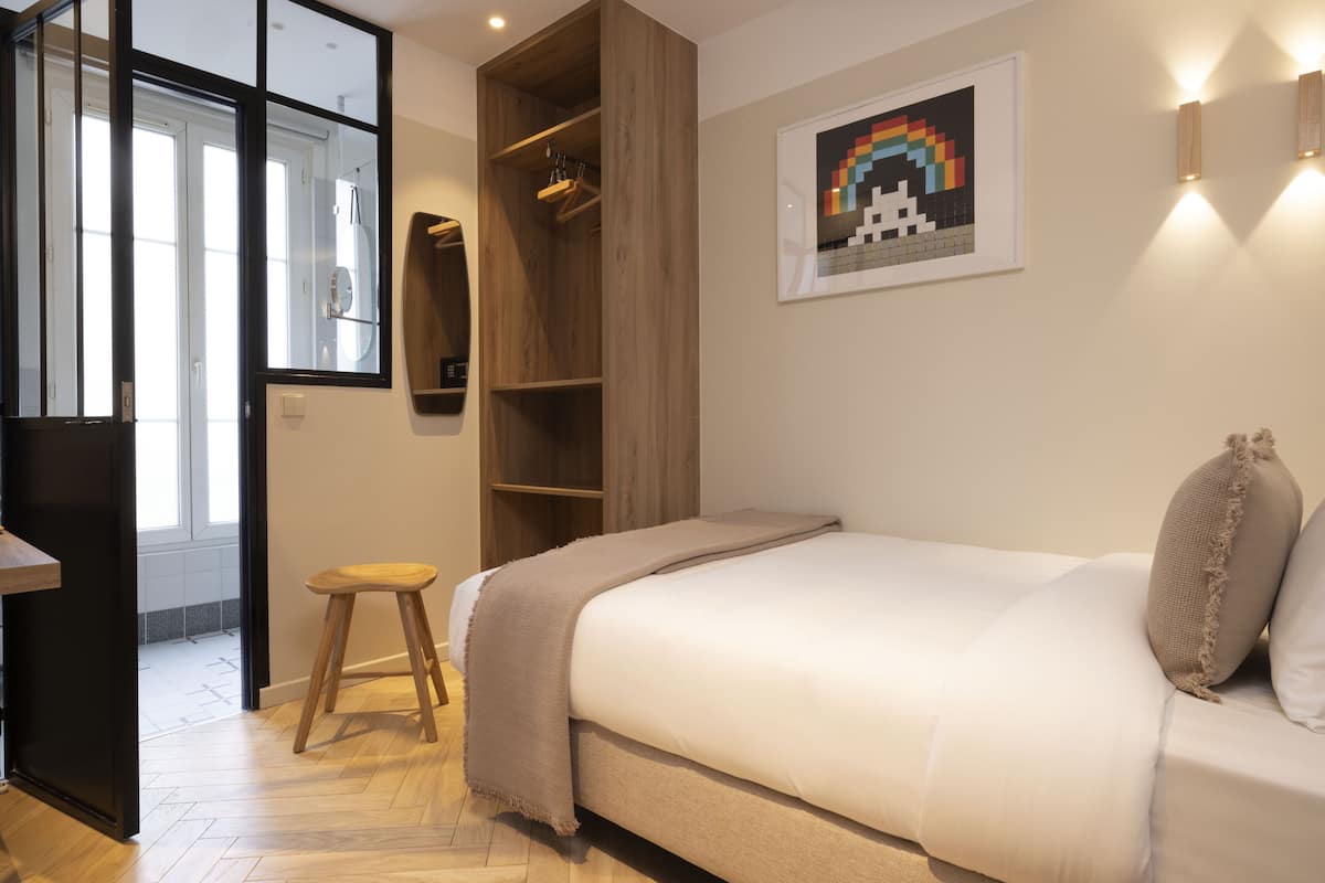 Ein Schlafzimmer mit Bett, einem Holzschemel, einem Kleiderschrank und einer Tür zu einem Badezimmer.