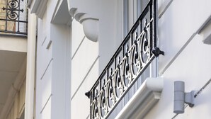 A building corner with a white facade, a black wrought iron balcony, and a window. - Le Daum (Paris)