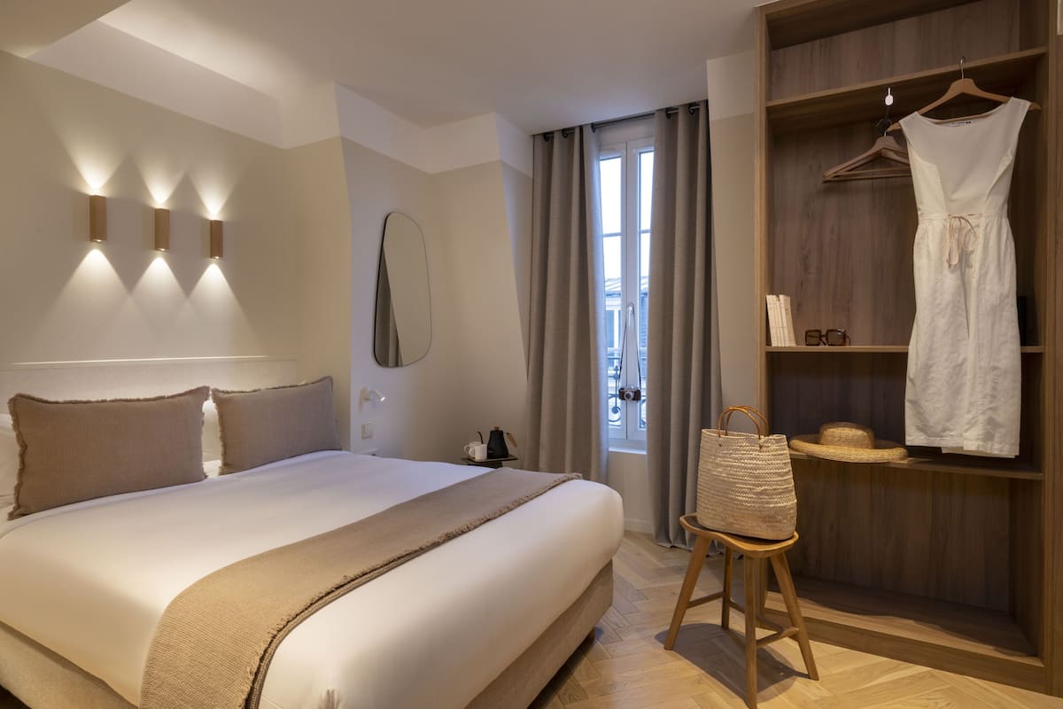 Ein ordentlich eingerichtetes Hotelzimmer mit einem großen Bett, einem Holzschrank und einem Kleiderschrank mit einem Kleid.