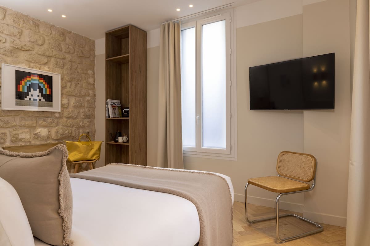 Ein Schlafzimmer mit Bett, Sessel, Fernseher, Bücherregal und Fenster.