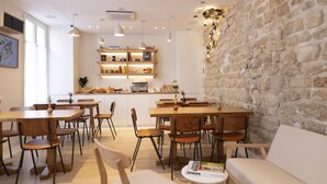 A modern dining area with wooden tables and chairs, a stone accent wall, and a kitchen in the background. - Le Daum (Paris)