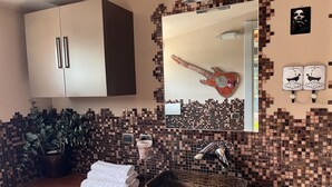 Ein Badezimmer mit gefliestem Rückspritzschutz, einem Waschbecken mit Wasserhahn, einem Spiegel, einem Handtuchhalter und einer dekorativen Gitarre.