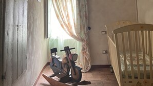 Ein rustikaler Raum mit Holzbalkendecke, einem Motorrad, einem Babybett und einem Fenster mit Vorhängen.