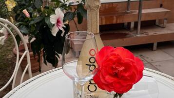 Une bouteille de vin Cristello, un verre et une rose rouge sur une table blanche, à l’extérieur.