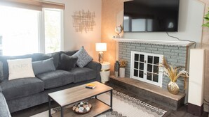 Un salón con sofá gris, una mesa de centro, chimenea y televisor de pantalla plana montado arriba.