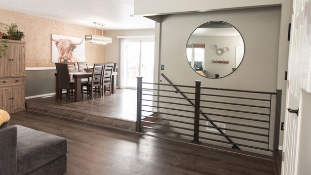 Un interior moderno con comedor, escalera y un espejo grande.