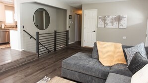 Una sala de estar con un sofá gris, una mesa de centro y una escalera con barandilla negra que lleva a otra habitación.