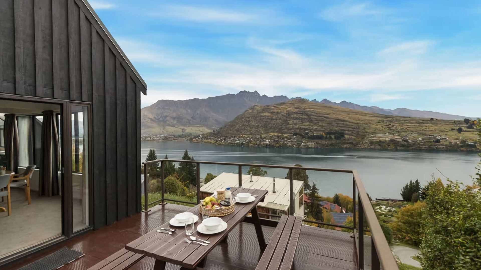 Terraza de madera con una mesa lista para comer, con vista a un lago y montañas.