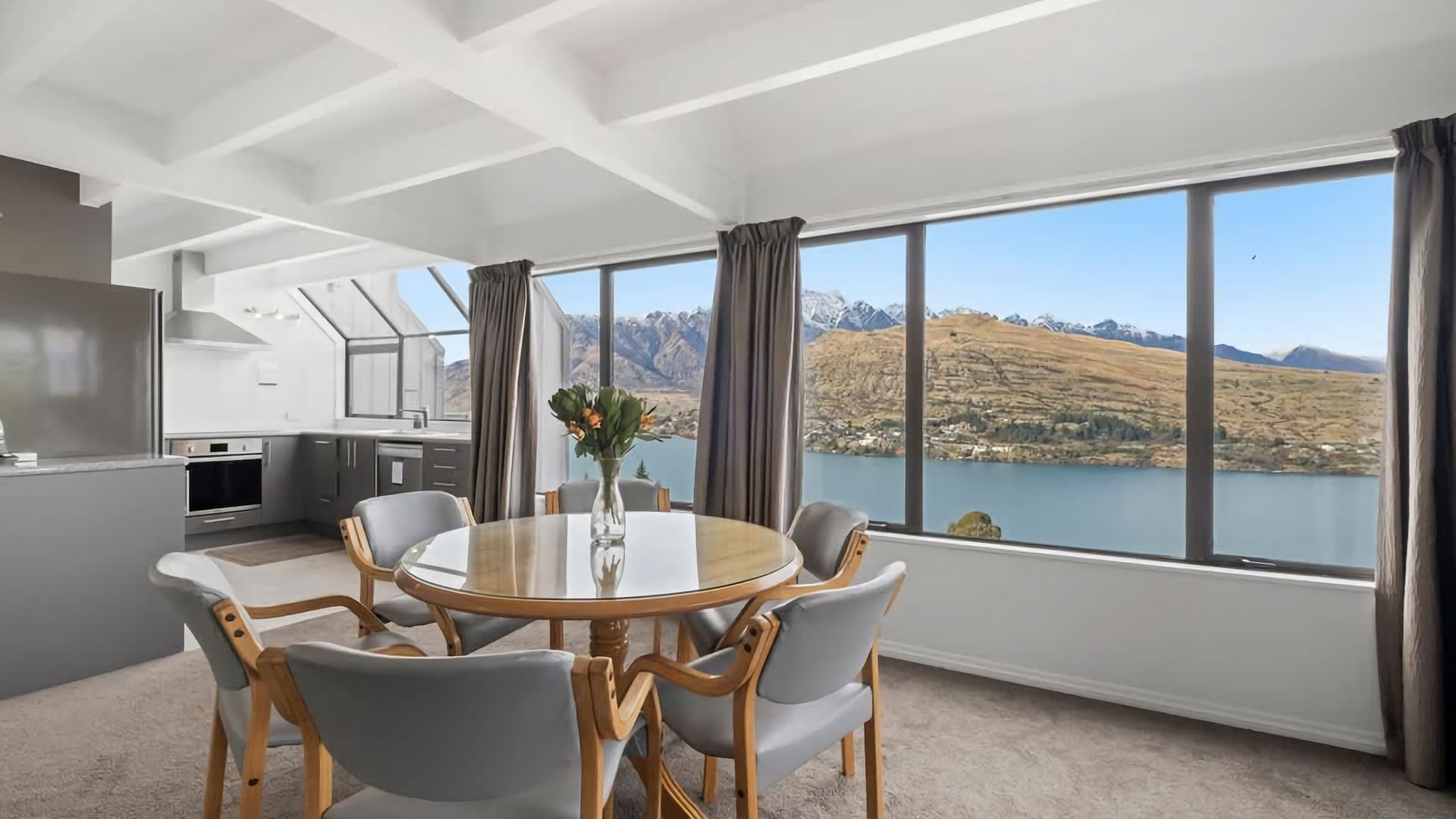 A modern kitchen with white cabinets and a large window overlooking a lake and mountains.