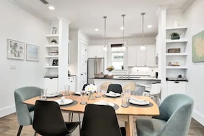 Cozinha moderna com armários brancos, uma mesa de jantar posta para quatro pessoas e iluminação pendente.