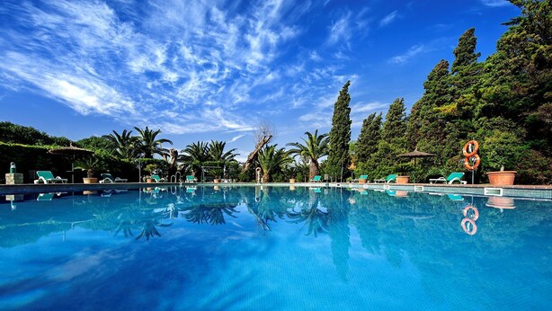 A clear blue pool with lounge chairs and palm trees in the background. - Hotel Punta Sur (Tarifa)