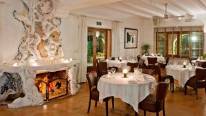 A restaurant with round tables, chairs, a fireplace, and large windows. - Hotel Punta Sur (Tarifa)
