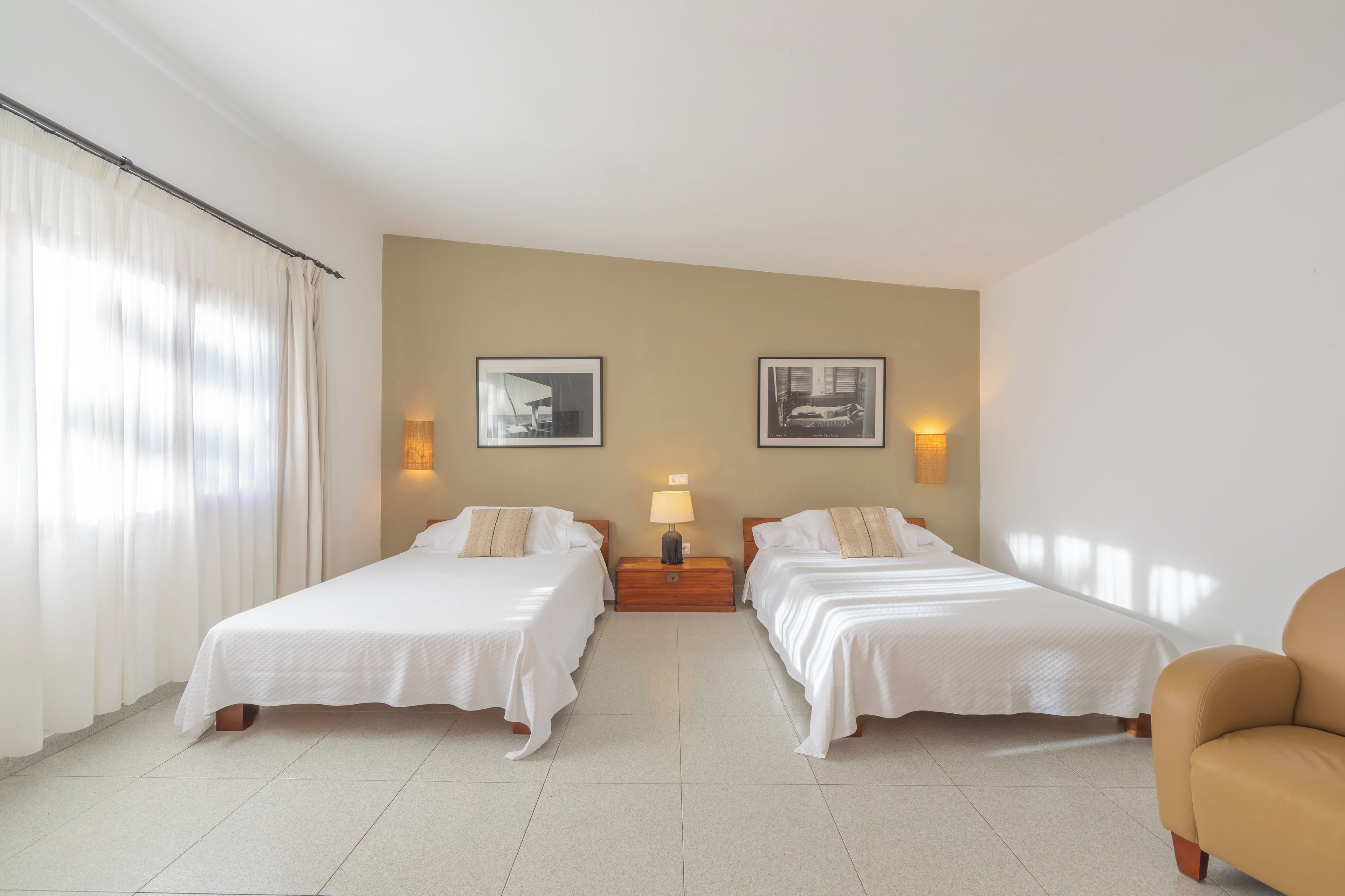Habitación de hotel con dos camas, una mesita de noche con lámpara y dos cuadros en la pared.