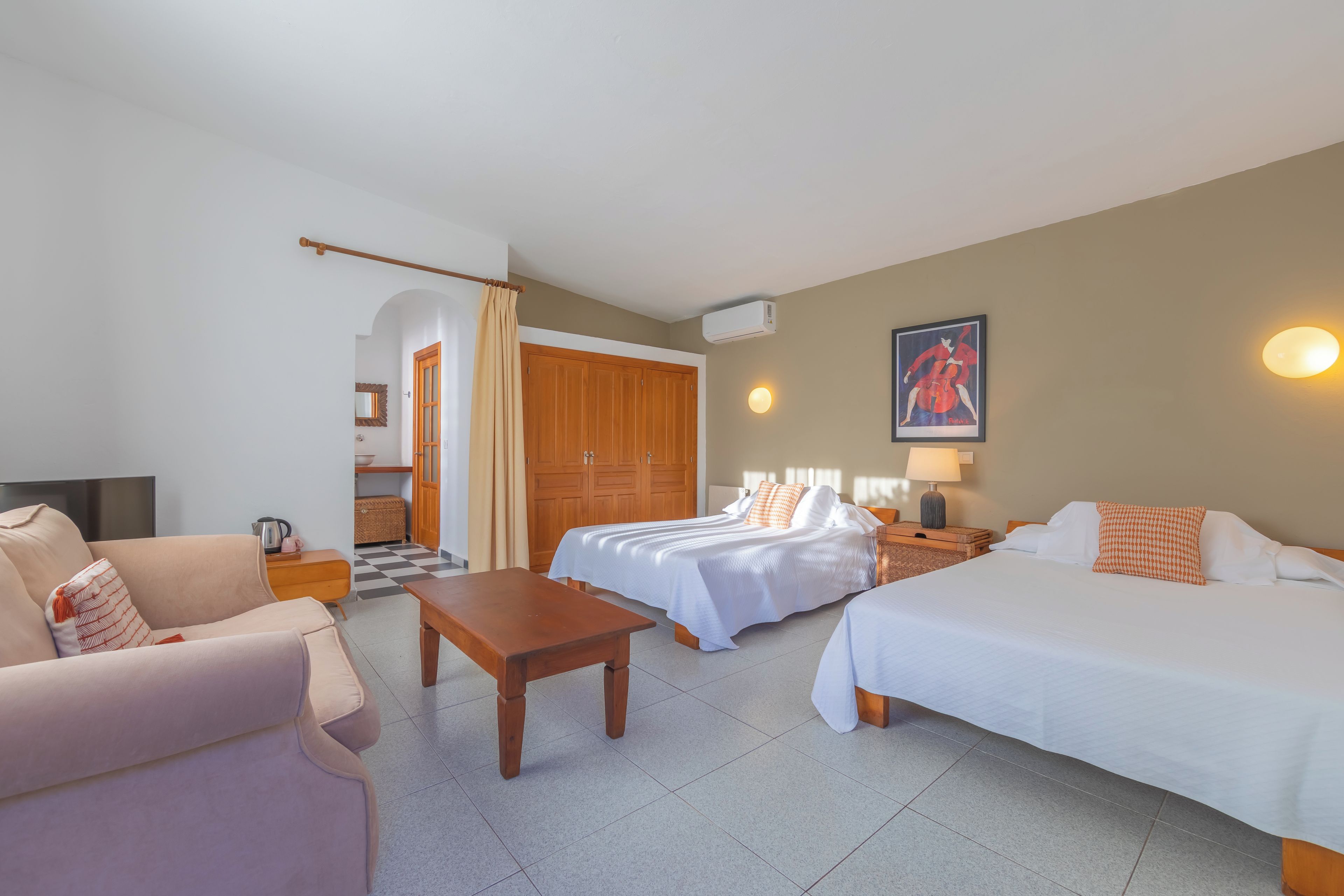 Habitación de hotel con dos camas, un sofá, una mesa y una zona de cocina al fondo.