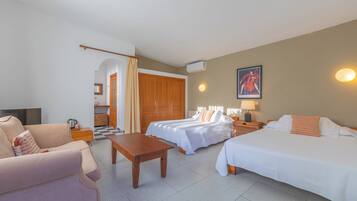 Habitación de hotel con dos camas, un sofá, una mesa y una zona de cocina al fondo.