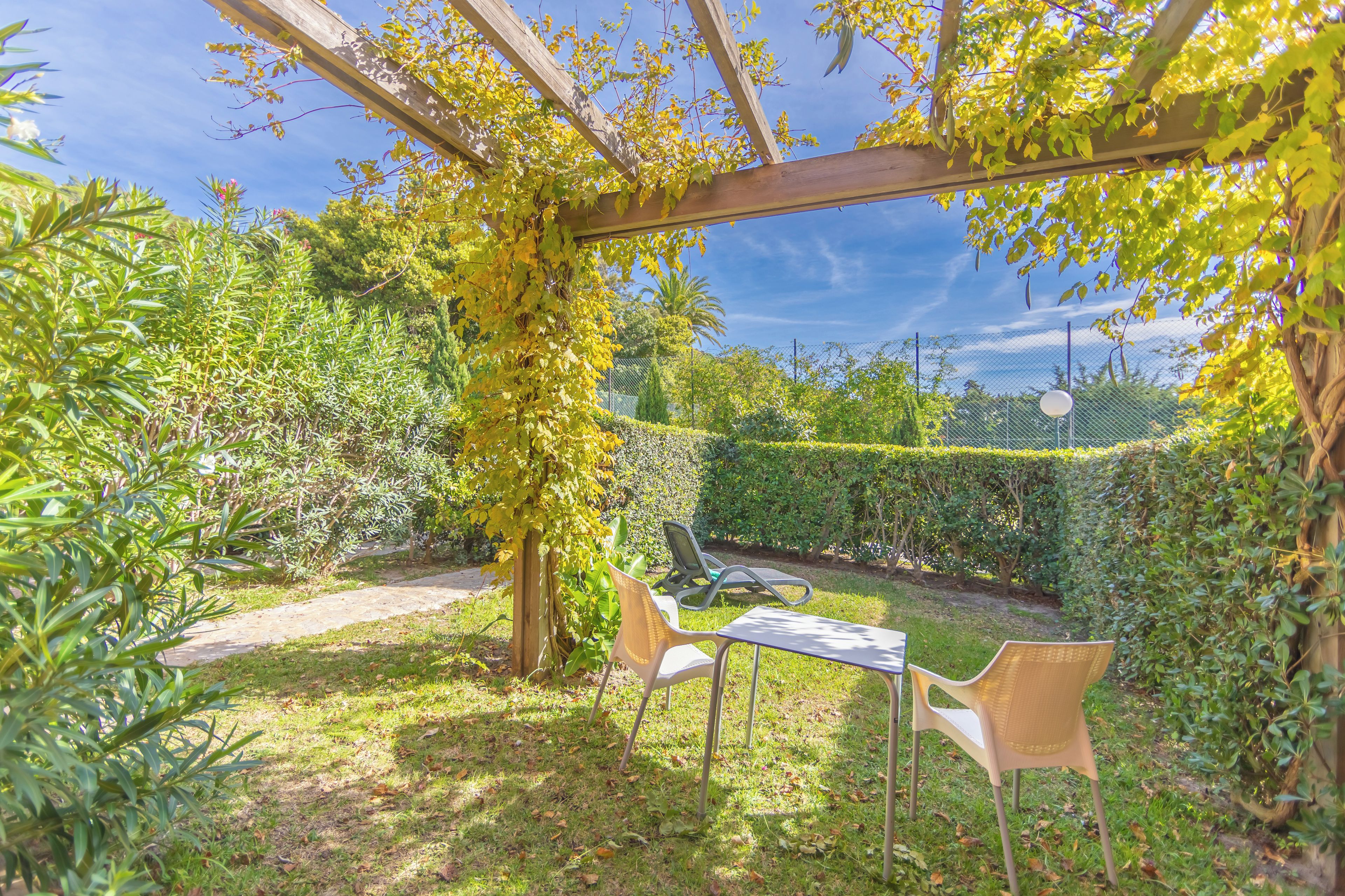 Un jardí amb una pèrgola, dues cadires i una taula.