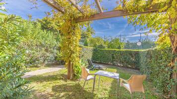 Un jardí amb una pèrgola, dues cadires i una taula.