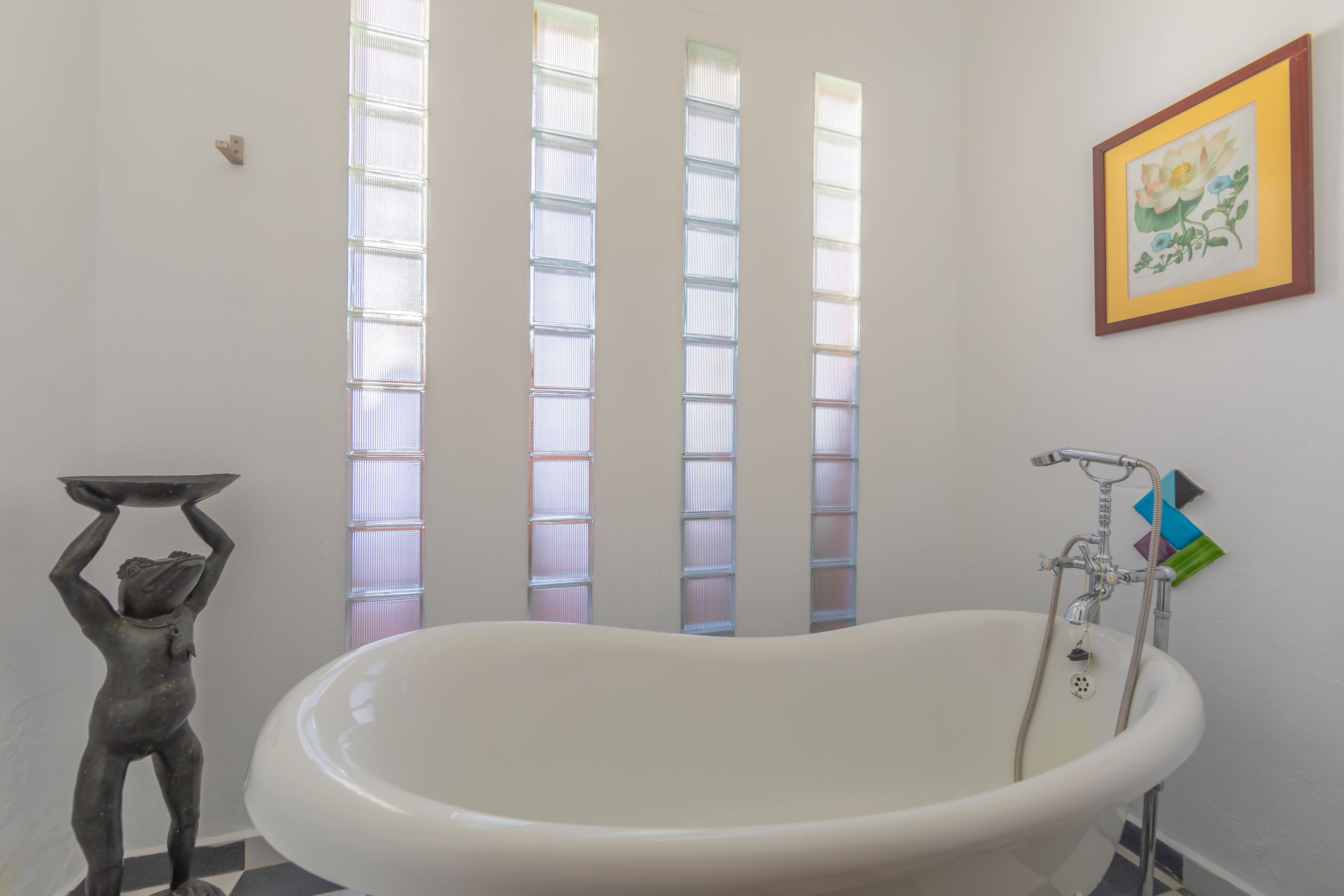 A bathroom with a freestanding bathtub, a wall-mounted toilet, and a window with frosted glass panels.