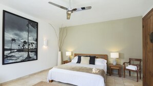 A bedroom with a large bed, two bedside tables with lamps, a wooden wardrobe, a ceiling fan, a large framed picture on the wall, and a woven rug. - Hotel Punta Sur (Tarifa)