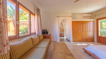 Una habitación con sofá, una mesa de madera, televisor y vistas al exterior.