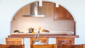 Uma cozinha com porta em arco, armários de madeira, coifa de aço inoxidável e um espaço de refeições com cadeiras de madeira e um vaso com flores.