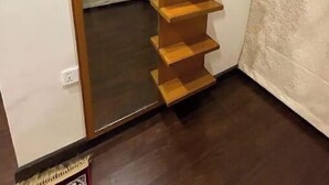 Une pièce avec une étagère en bois adossée à un mur, une porte donnant sur une autre pièce et un rideau recouvrant partiellement une fenêtre.
