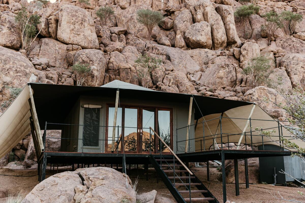 A tented accommodation with a staircase leading to a door, set against a rocky hillside.