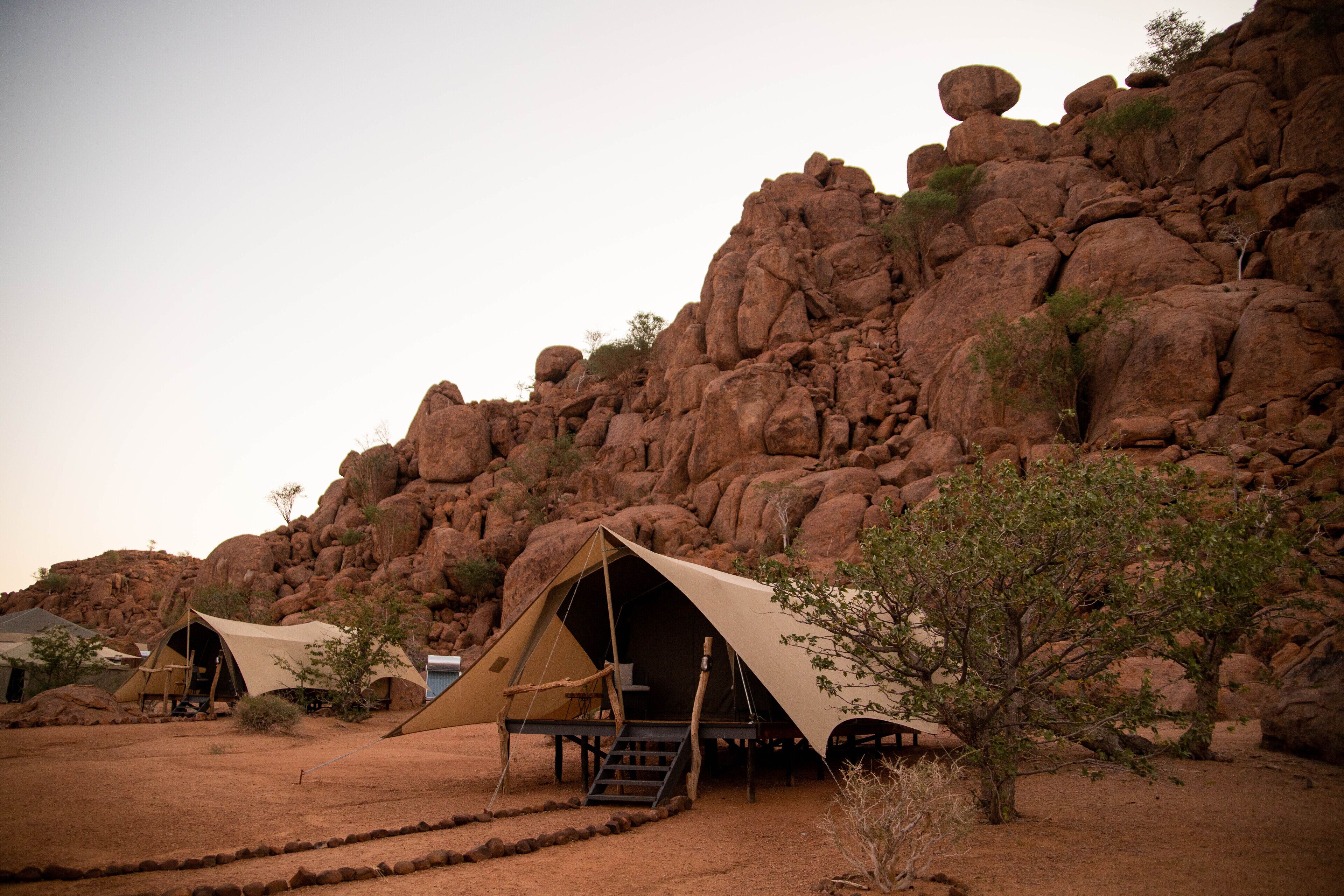 A desert campsite with tents set up on a flat area, surrounded by rocky terrain and sparse vegetation.