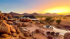 Un resort en el desierto con terraza al aire libre, piscina y vistas a las montañas.