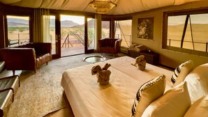 Amplia habitación con una cama grande, dos sillones, una mesa de comedor y vistas al paisaje desértico.