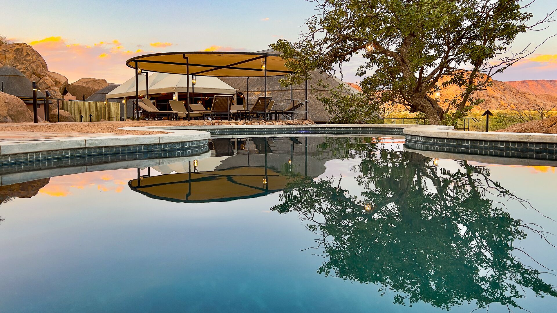 A pool with a sunken center, surrounded by lounge chairs and a covered seating area.