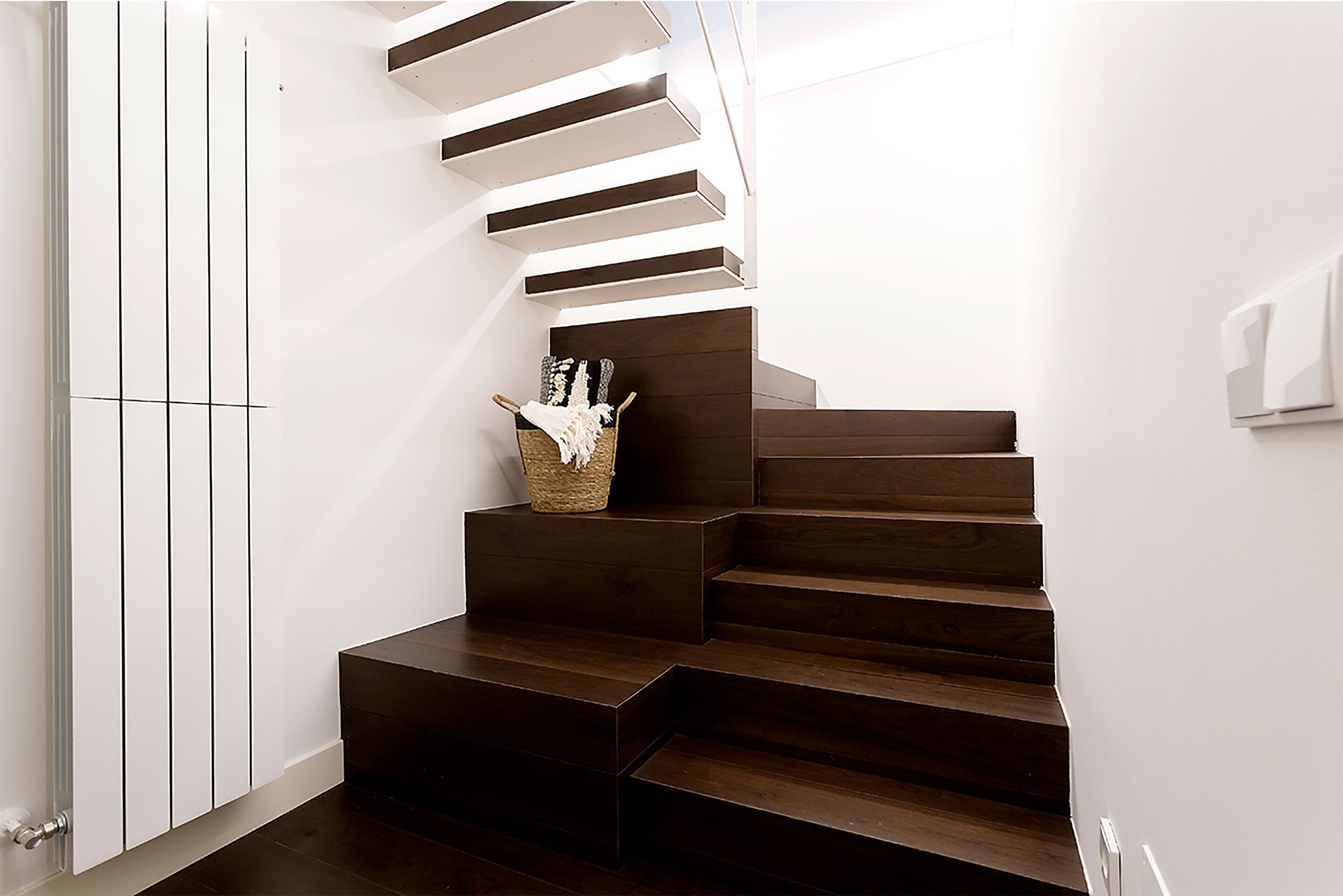 Una escalera moderna con escalones de madera oscura y paredes blancas.