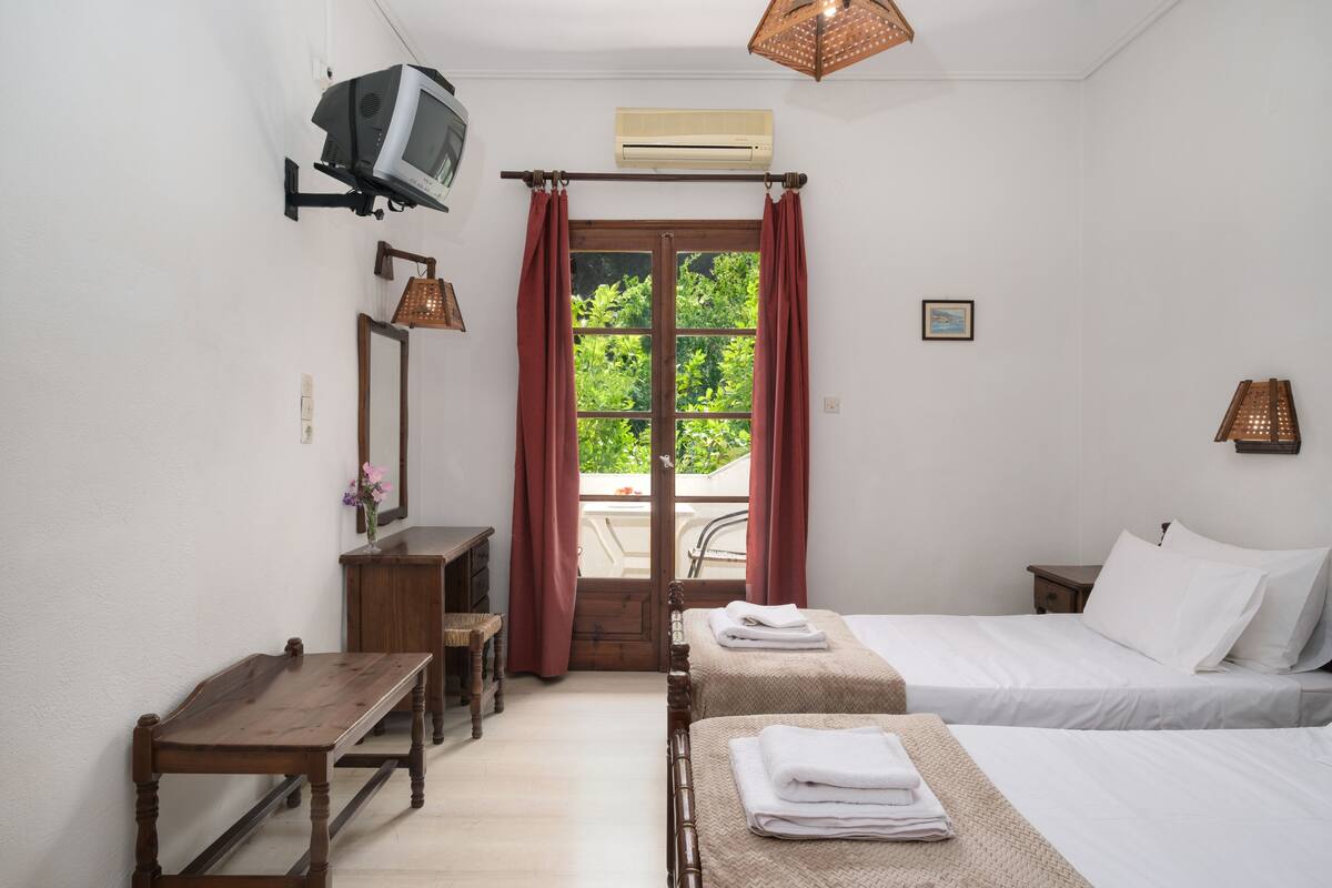 Ein Schlafzimmer mit zwei Betten, einem Holztisch, einem an der Wand montierten Fernseher und einem Fenster mit roten Vorhängen.