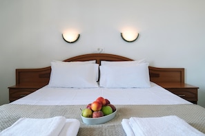 A neatly made bed with white linens, a bowl of fruit on the bed, and two wall-mounted lights. - Koukounaries Beach Hotel (Skiathos)