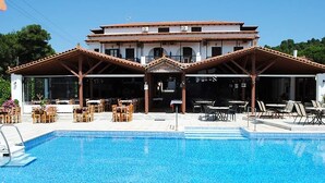 A hotel with a swimming pool, outdoor seating, and a traditional architectural style. - Koukounaries Beach Hotel (Skiathos)