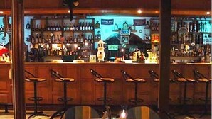 A bar area with multiple stools and a round table with a candle. - Koukounaries Beach Hotel (Skiathos)