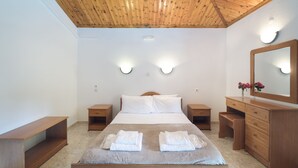 A bedroom with a wooden ceiling, a bed with white linens, two bedside tables, a dresser, and wall-mounted lights. - Koukounaries Beach Hotel (Skiathos)