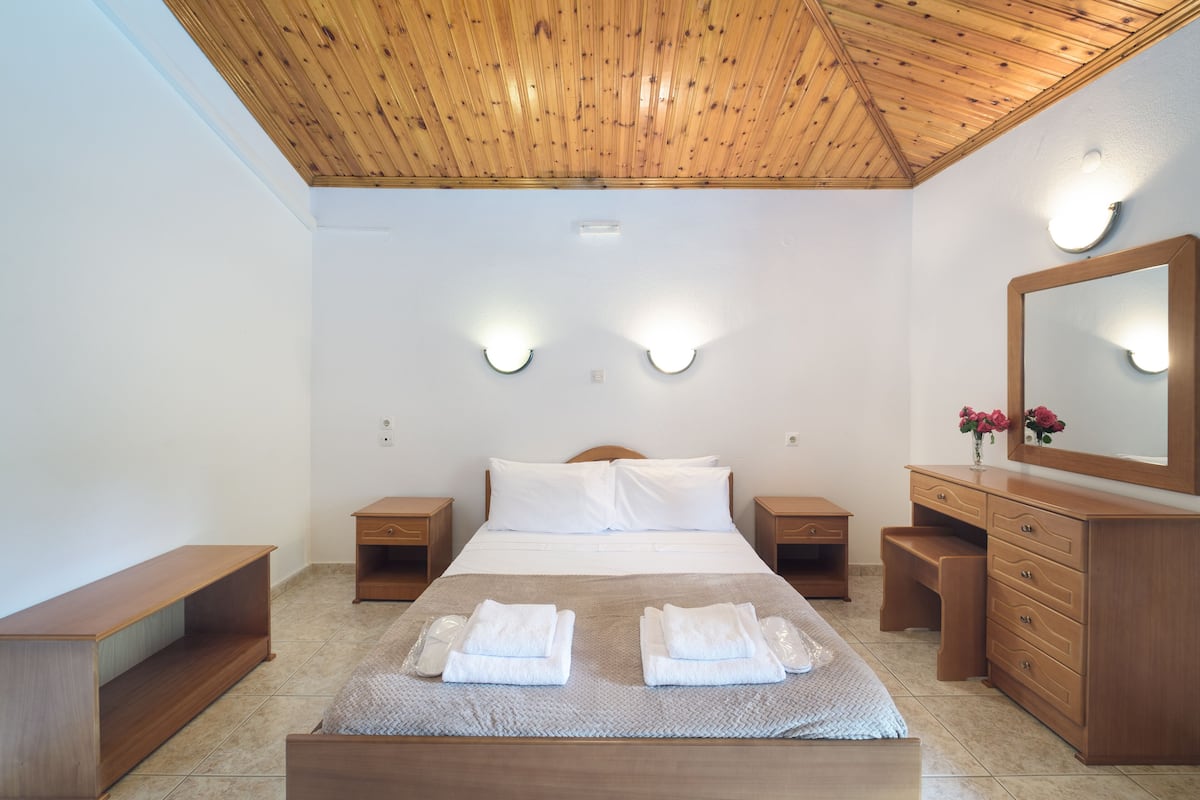 Ein Schlafzimmer mit Holzboden, einem Bett mit weißen Leinen, zwei Nachttischen, einer Kommode und Wandleuchten.
