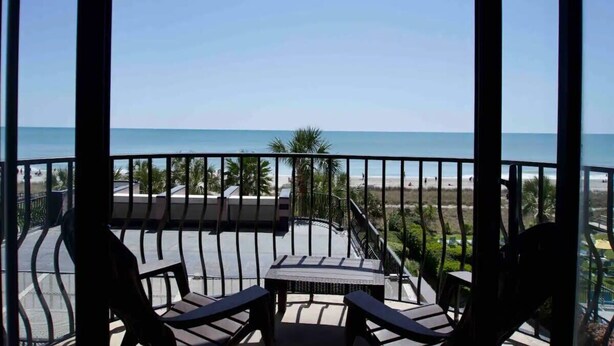 A balcony with a view of the beach, equipped with outdoor furniture and a table. - Great Ocean Front Condo in Heart of Myrtle Bech (Myrtle Beach)