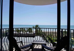 A balcony with a view of the beach, equipped with outdoor furniture and a table.