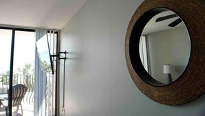 A room with a large round mirror on the wall, a sliding glass door leading to a balcony, and a chair on the balcony. - Great Ocean Front Condo in Heart of Myrtle Bech (Myrtle Beach)