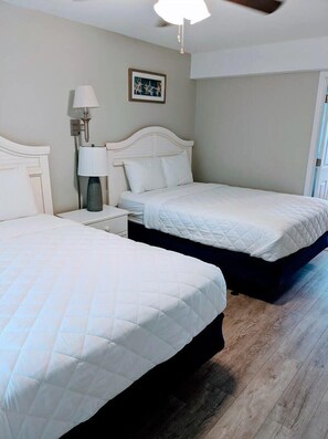 Une chambre avec deux lits, une table de chevet avec une lampe et un ventilateur de plafond.