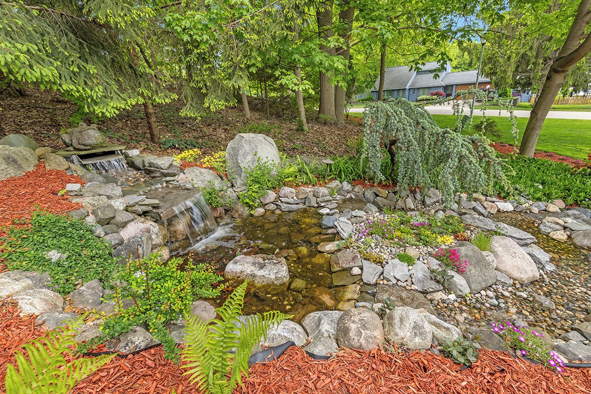 A garden with a small waterfall, surrounded by rocks and various plants.