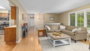 Uma sala de estar moderna com um sofá modular, uma mesa de centro e uma cozinha ao fundo.