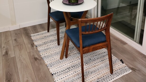A dining area with a round table, two chairs, and a decorative rug.