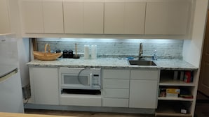 A compact kitchen with white cabinets, a granite countertop, a microwave, and a sink.