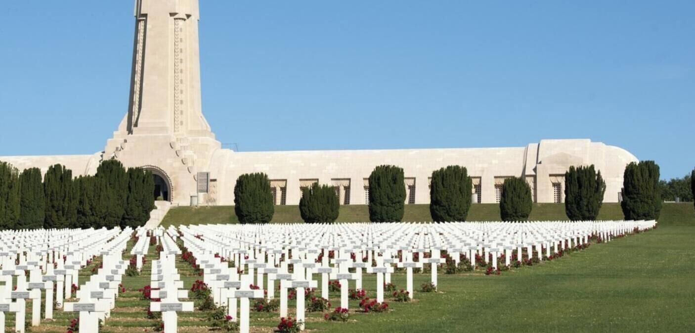 Un cimetière avec des pierres tombales blanches et un grand bâtiment en arrière-plan.