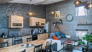Una cocina moderna con armarios de madera, un comedor con mesa y sillas de madera, y un rincón de estar acogedor con cojines.