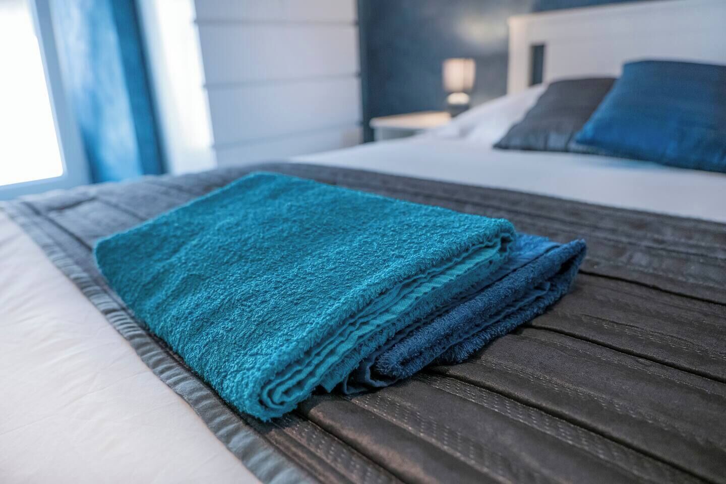 Una cama bien hecha con una toalla azul doblada y un cabecero de madera.