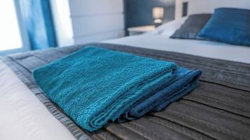 Una cama bien hecha con una toalla azul doblada y un cabecero de madera.